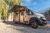 RV rental camper van with extended awning and open door showing modern interior, parked on gravel.