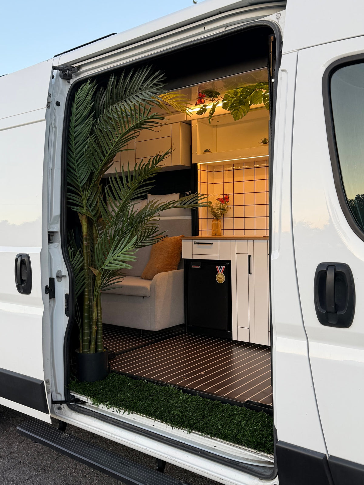 Modern RV rental: See inside a custom van's open door, revealing a compact kitchen, sofa, and artificial plants for a cozy interior. — photo 13