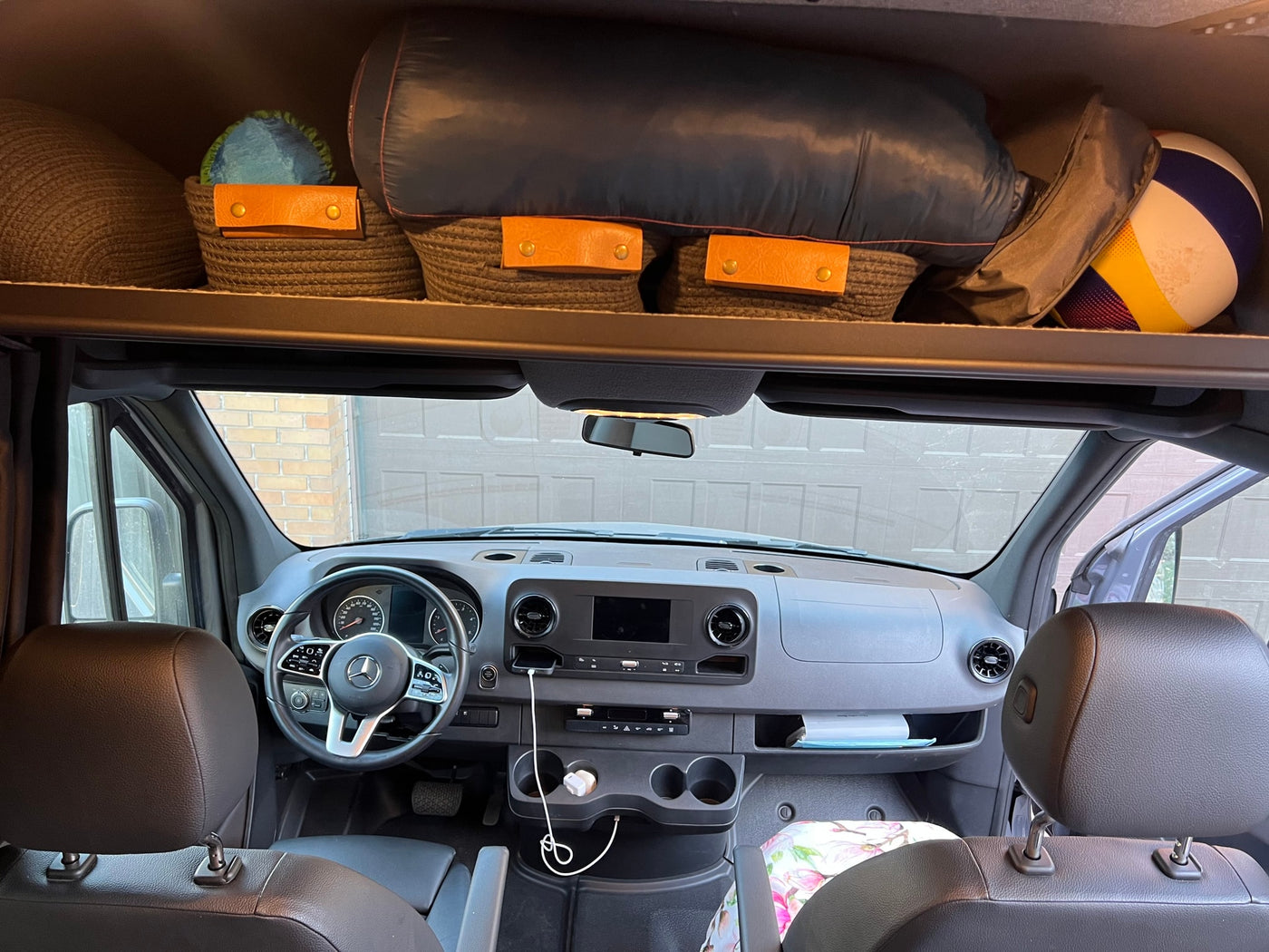 RV rental interior: Mercedes van cabin with dashboard, phone charging, & organized overhead storage for gear and baskets. — photo 9