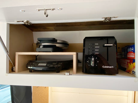 RV rental kitchen cabinet with Cuisinart toaster, waffle maker, and NuWave induction cooktop. Custom shelving & secure latches.