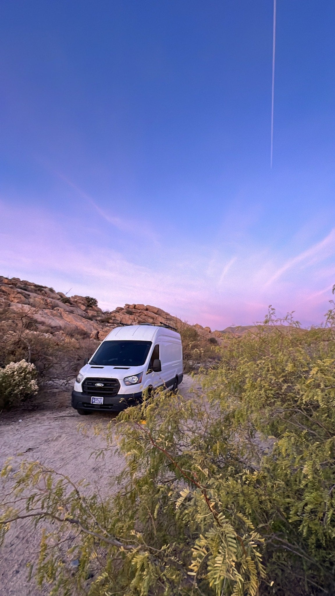 Experience desert van life with our RV rental! White camper van parked on a dirt road at sunset in a rocky landscape.|White Ford Transit rv rental van overlooking majestic snow-capped mountains