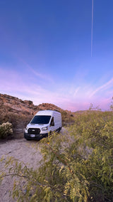 Experience desert van life with our RV rental! White camper van parked on a dirt road at sunset in a rocky landscape.