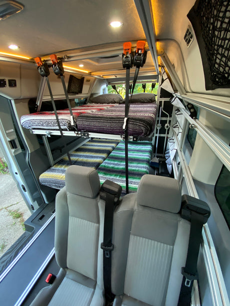 An RV rental van interior features a double bunk bed system with vibrant blankets, along with rear passenger seats, ideal for travel.