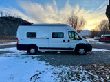 White Winnebago Solis camper van for RV rental, parked in a snowy setting with a sunset over mountains.
