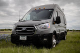 A gray Ford Transit van, ideal for RV rental, parked in a green field under cloudy skies.