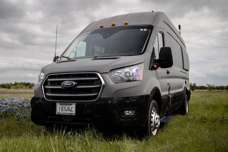 A gray Ford Transit van, ideal for RV rental, parked in a green field under cloudy skies.