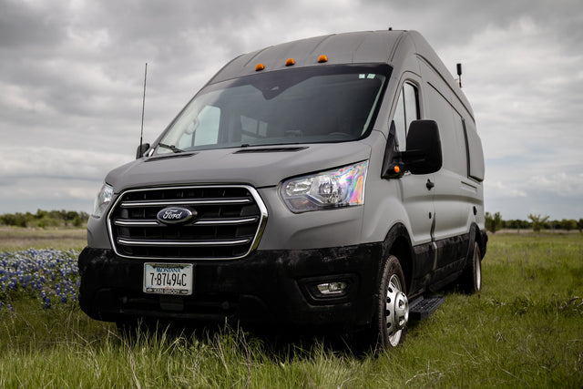 A gray Ford Transit van, ideal for RV rental, parked in a green field under cloudy skies.
