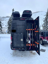 An RV rental camper van's custom rear storage, open to show organized skis, snowboards & poles. Thule/Yakima roof boxes visible.