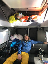 Inside an rv rental: child reading on an upper bunk, adult relaxes on the lower seat. A cozy, adventure-ready living space.