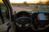 Inside an RV rental: driver's view of the Mercedes-Benz dashboard, infotainment screen, and sunset road ahead.