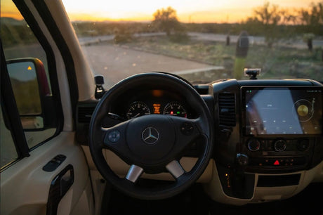 Inside an RV rental: driver's view of the Mercedes-Benz dashboard, infotainment screen, and sunset road ahead.