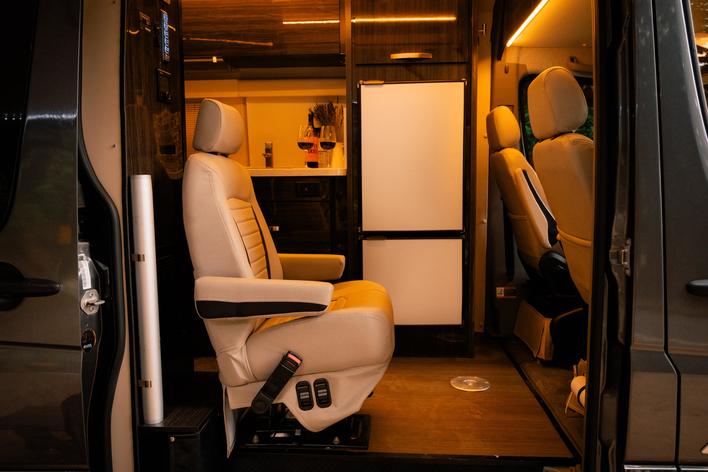 Inside a luxury RV rental: plush beige captain's chair, modern kitchen with fridge, and warm lighting. Ready for adventure! — photo 11