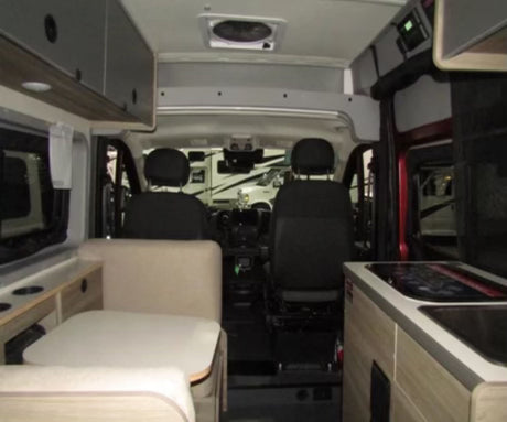 Interior of a spacious rv rental: cockpit upfront, with a dinette on the left and compact kitchen on the right.
