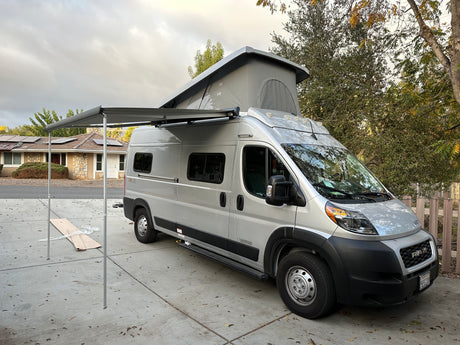 Silver camper van RV rental with a pop-top and extended awning, parked on a driveway, ready for adventure.