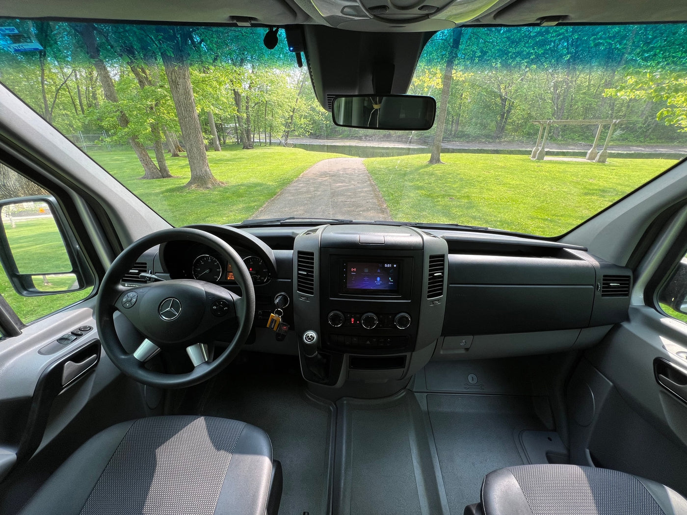 Inside a spacious RV rental, a clear view of a scenic park path with green trees and grass awaits your adventure. — photo 19