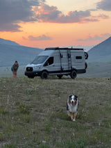 Embrace van life! An RV rental, a woman, and her happy dog at sunset in the mountains. Perfect for outdoor adventures.
