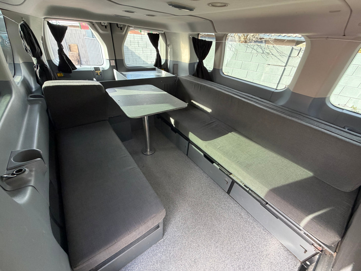 RV rental camper van interior featuring grey bench seating, a central table, under-seat storage, and privacy curtains.
