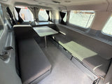 RV rental camper van interior featuring grey bench seating, a central table, under-seat storage, and privacy curtains.