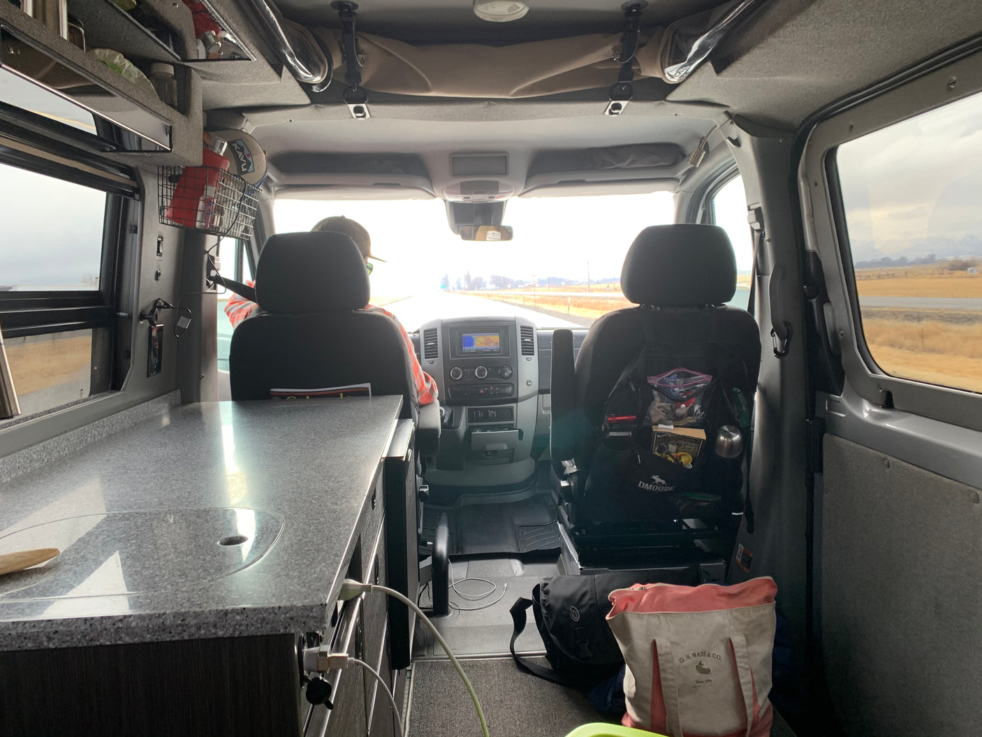 Inside an RV rental traveling down the highway, showing the driver, passenger seat, and kitchen counter.
