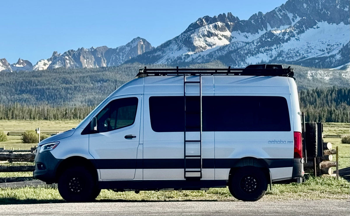 A silver RV rental camper van with roof rack and ladder