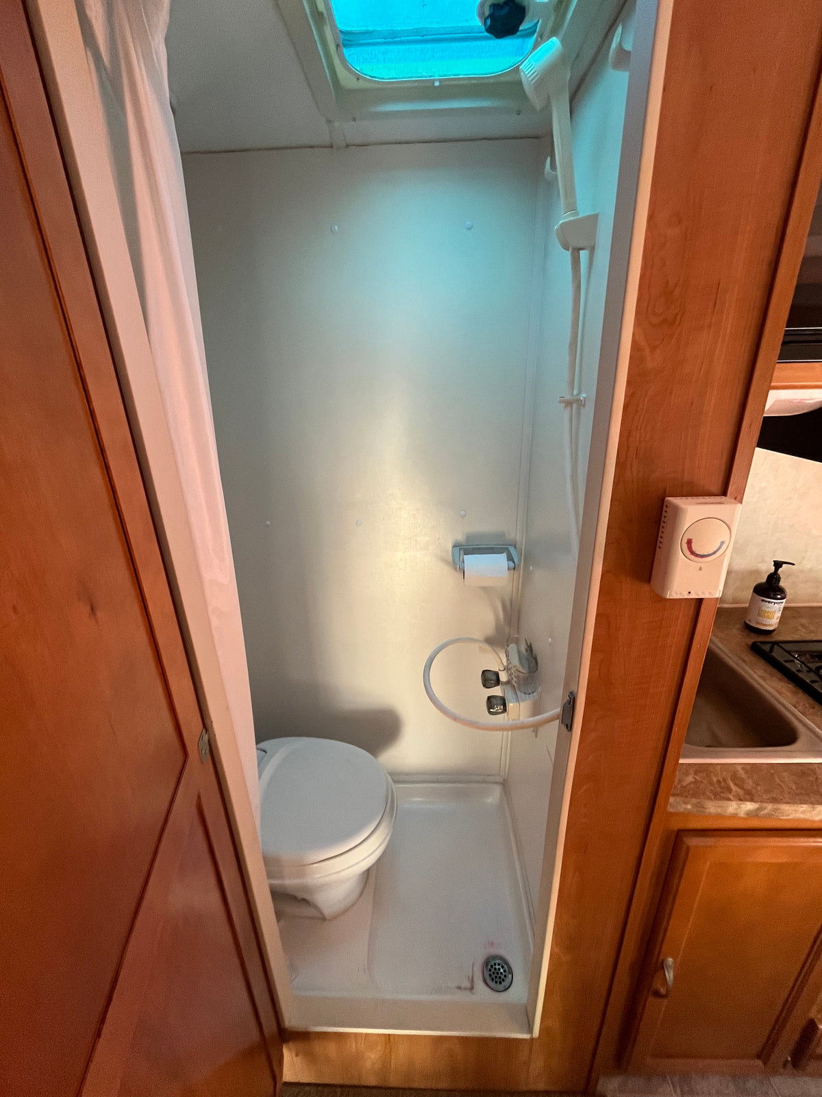 Compact RV rental wet bath, featuring a toilet, shower head, and overhead skylight for travel convenience. — photo 4