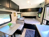 Comfortable RV rental interior showcasing a cozy bed, dinette, and sleek overhead cabinets. Perfect for trips!