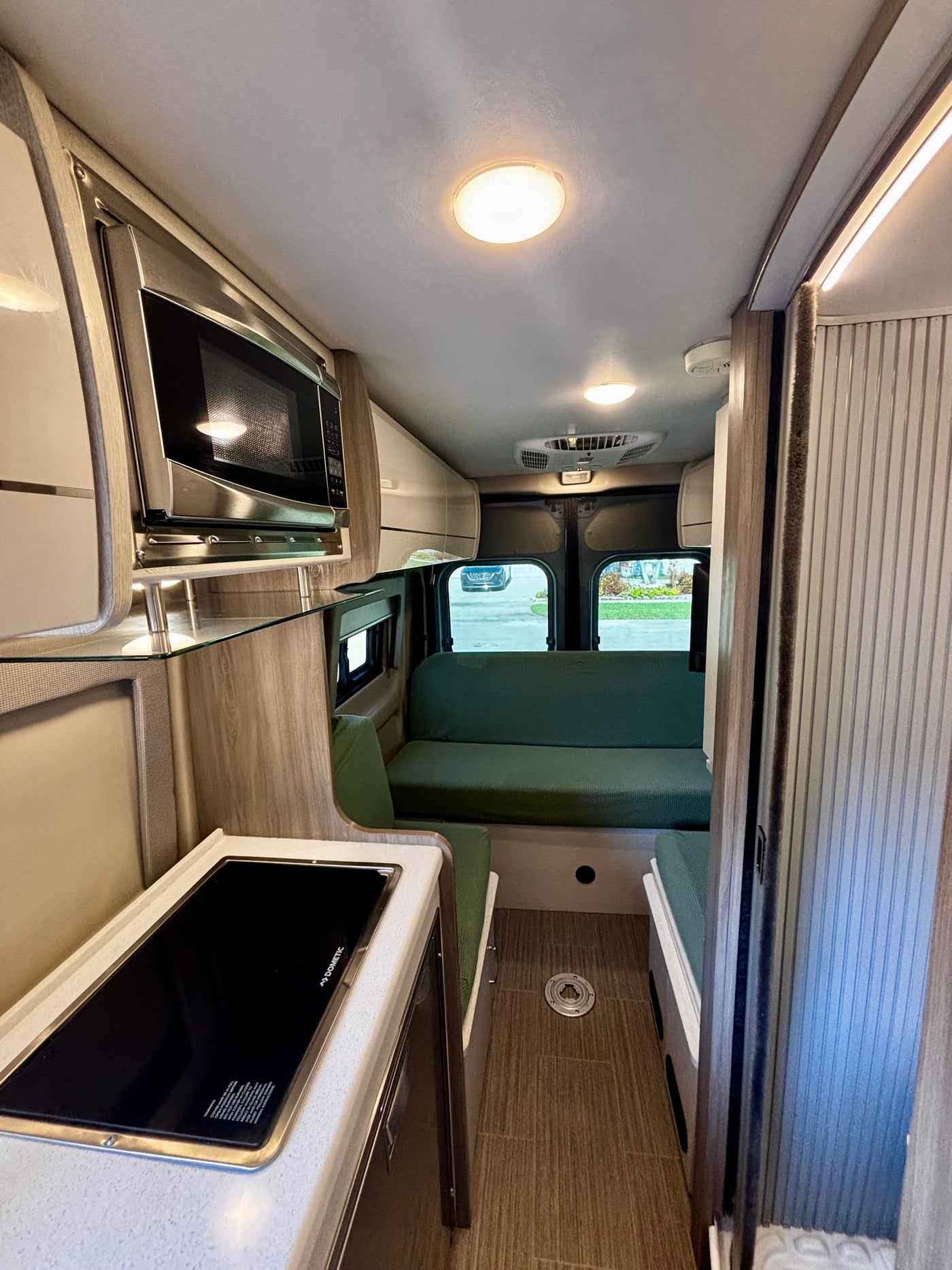 Spacious RV rental interior with kitchen amenities like microwave and Dometic cooktop, cozy green seating, and bright lighting. — photo 13