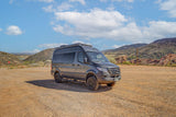 Explore the outdoors! This off-road ready gray rv rental van is parked on a dirt lot amidst scenic mountains.