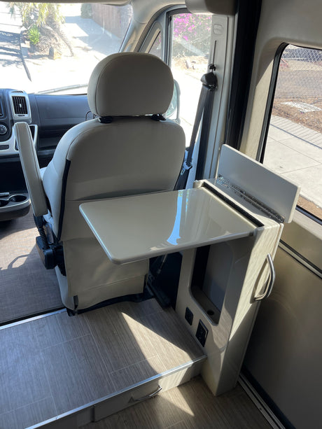 An rv rental's interior: passenger seat swiveled to face a compact table and side console with power outlets for convenience.