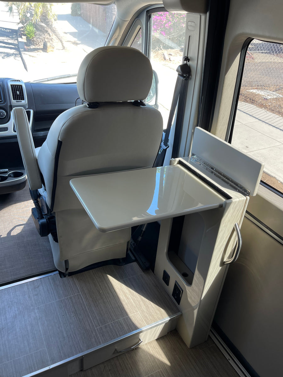 An rv rental's interior: passenger seat swiveled to face a compact table and side console with power outlets for convenience.