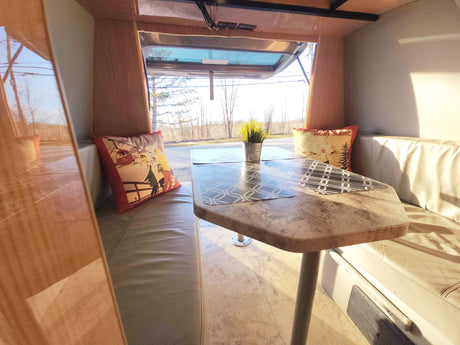 Cozy RV rental dinette with open window view, perfect for road trips. Features comfortable seating and a table.