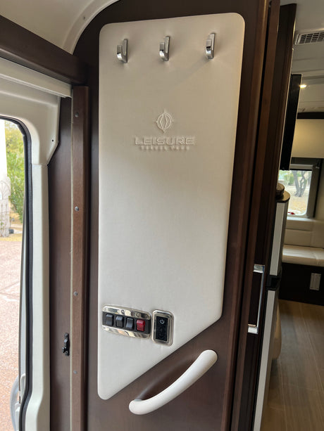 RV rental entry: Beige padded panel with chrome hooks, 'Leisure Travel Vans' logo, control switches, and white grab handle.