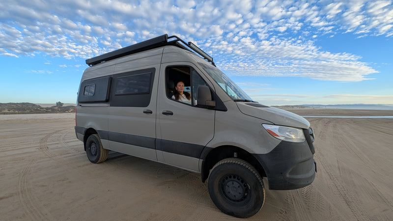 Exploring coastal dunes in an RV rental! A custom camper van on sand, with a woman at the wheel under a cloud-filled sky. — photo 2