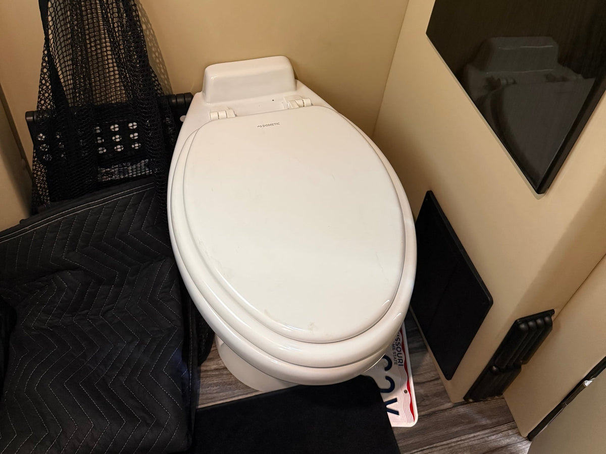  looking out at a garage and trees.|Luxurious cream leather captain's chairs inside an RV rental conversion van with a wood floor and open sliding door.|Black Nov Kool compact refrigerator — photo 7