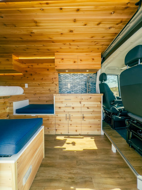 Explore this bright RV rental with warm wood walls, functional kitchenette, and clever sleeping solutions for your travels.