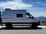 Silver Winnebago Revel camper van for rv rental, parked on a road with snowy mountains & blue sky. Perfect for adventure travel!