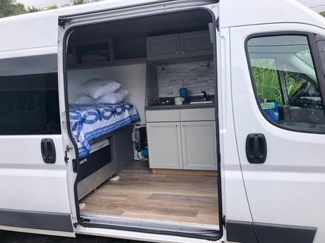 Bright rv rental camper van interior: cozy bed, compact kitchen, Dometic cooler. Ready for your next adventure.