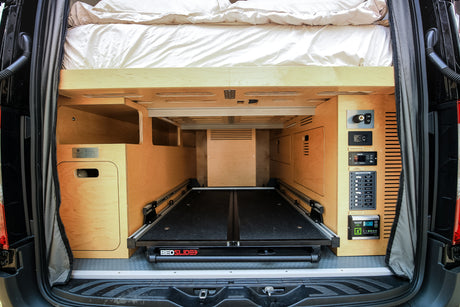 RV rental camper van's rear: bed, slide-out cargo tray, and control panels. Ideal for off-grid travel.