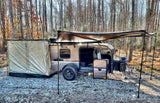 Explore nature with this RV rental setup: a teardrop camper with tent and awning at a wooded campsite.