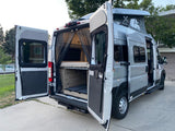 This silver RV rental camper van has its rear and side doors open, showcasing the interior bed, storage, and raised pop-top roof.