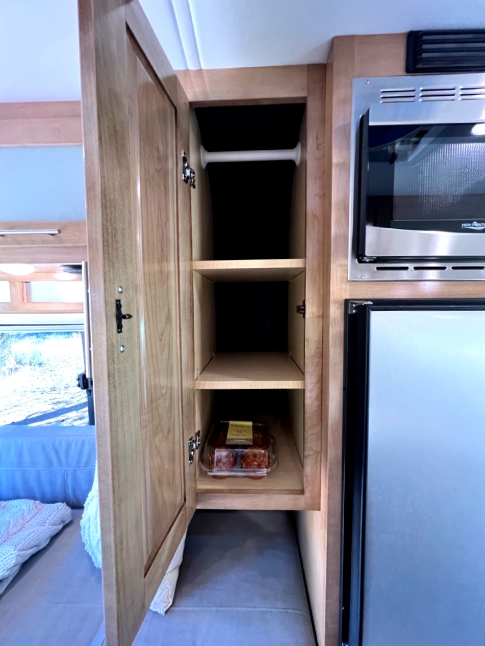 RV rental: Open wood cabinet shows shelves, baked goods, near microwave & fridge. Smart storage solutions. — photo 15