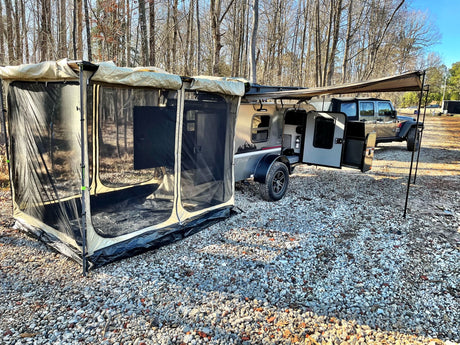 Compact rv rental: a teardrop camper trailer with an attached screen room and awning, on gravel, by a Jeep.