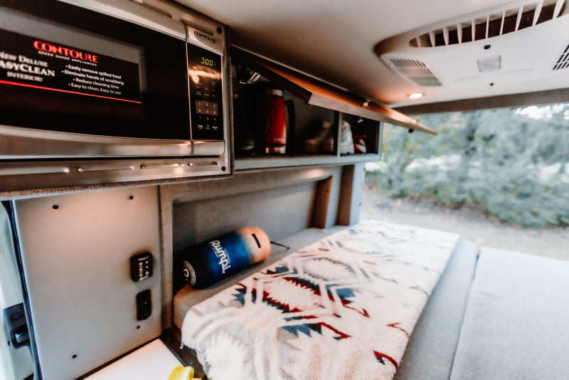  & blurred nature views from the window.|RV rental interior features a compact kitchen with a microwave — photo 7