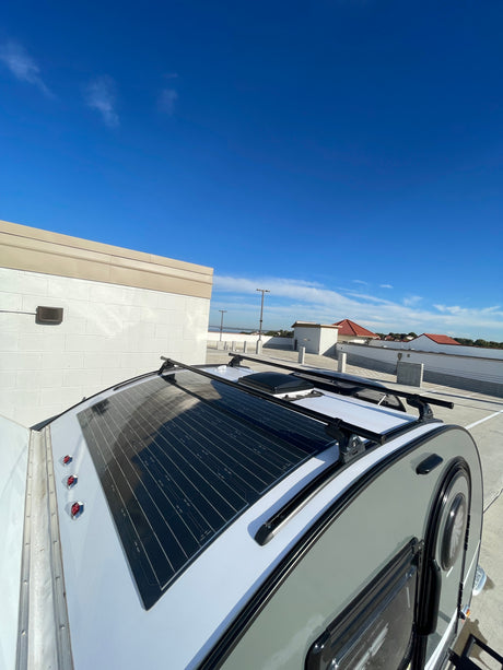 Top view of an rv rental travel trailer, equipped with a solar panel and roof racks, parked outside under a clear blue sky.