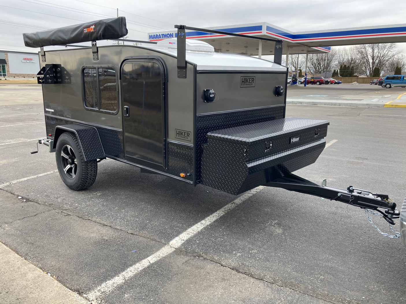Dark grey Hiker teardrop trailer, ideal for RV rental adventures. Features an awning and front storage box.