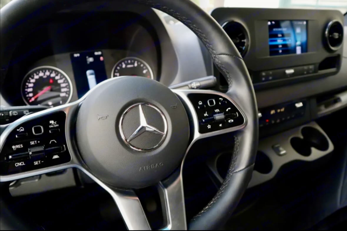 Inside your RV rental: Driver's cockpit of a Mercedes-Benz Sprinter, featuring a modern dashboard, steering wheel, and infotainment system.