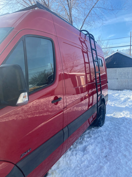 Red 2500 RV rental van, equipped with a roof ladder, parked in a snowy winter scene under a blue sky.