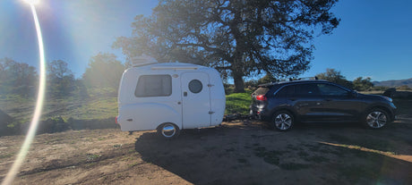 RV rental: White compact camper trailer and SUV parked on dirt under bright sun, ideal for exploring nature & road trips.