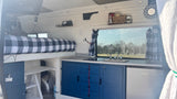 Cozy rv rental interior with elevated plaid bed, kitchenette, Hisense fridge, and window view.
