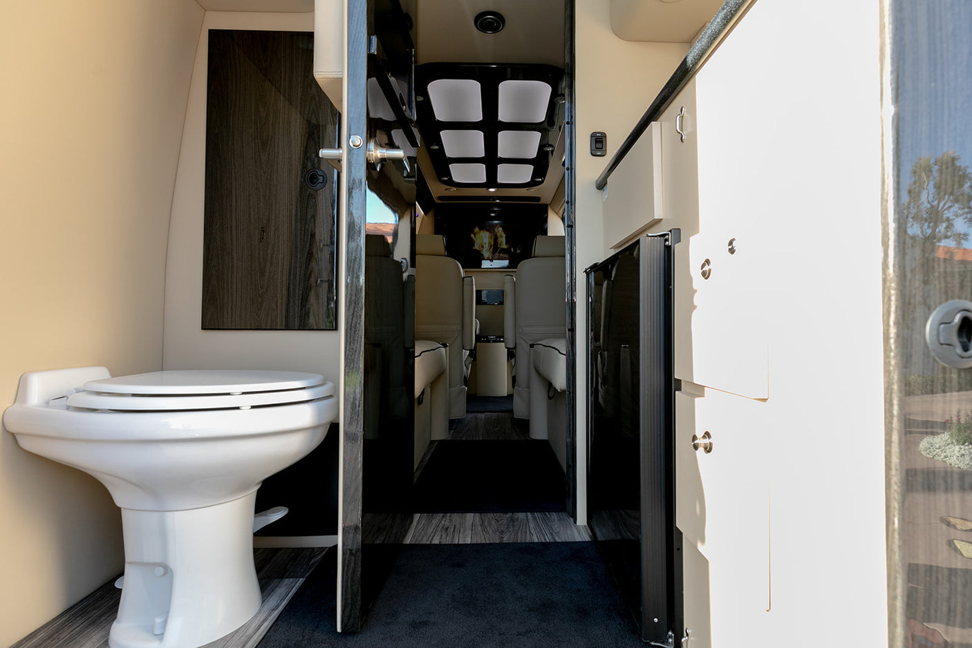 Luxury rv rental interior showing a sleek toilet on the left, cabinetry on the right, and comfortable passenger seating beyond.